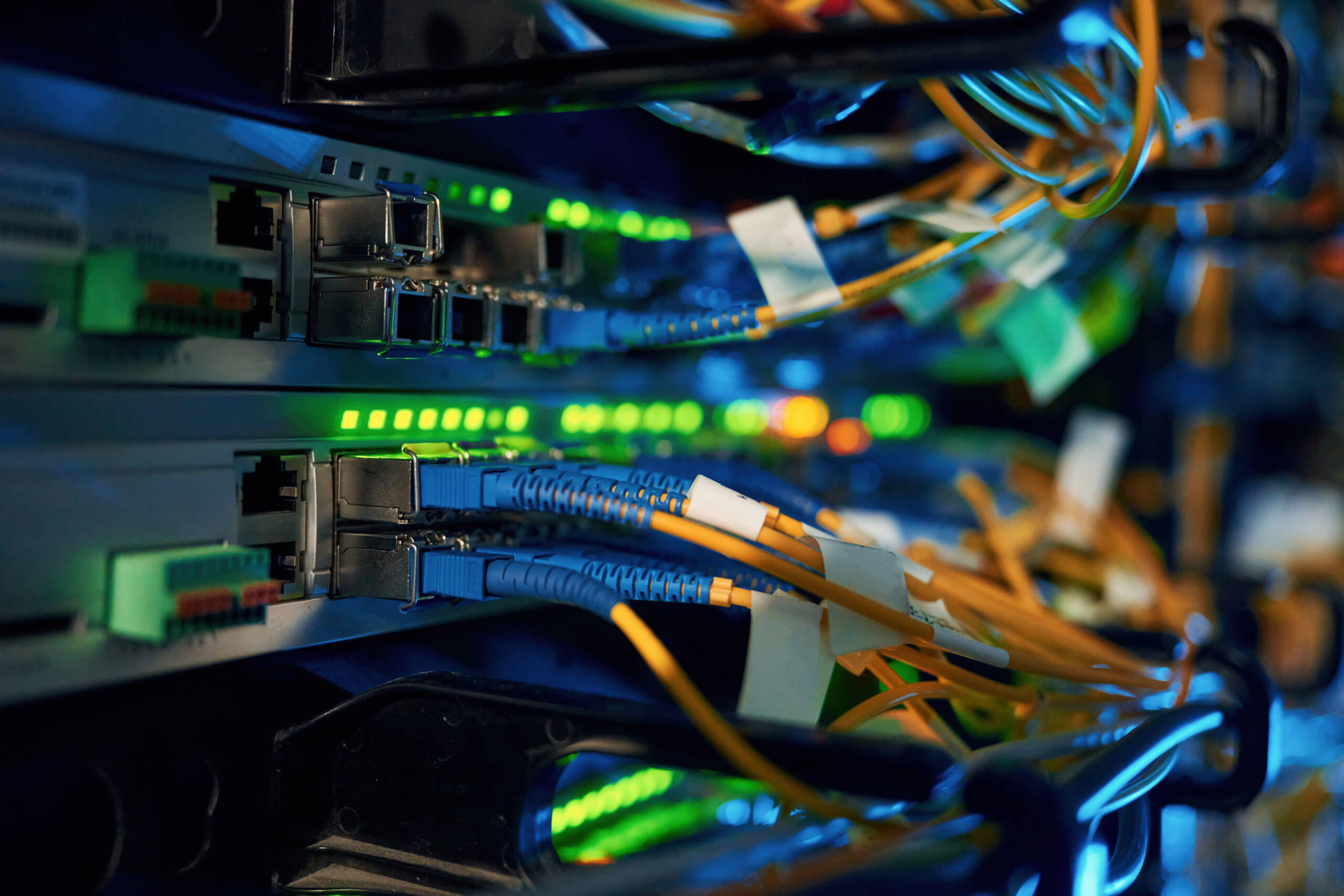 Nahaufnahme von Switches mit SFP-Modulen, angeschlossenen Glasfaser-Patchkabeln und grün leuchtenden Status-LEDs im Netzwerkschrank