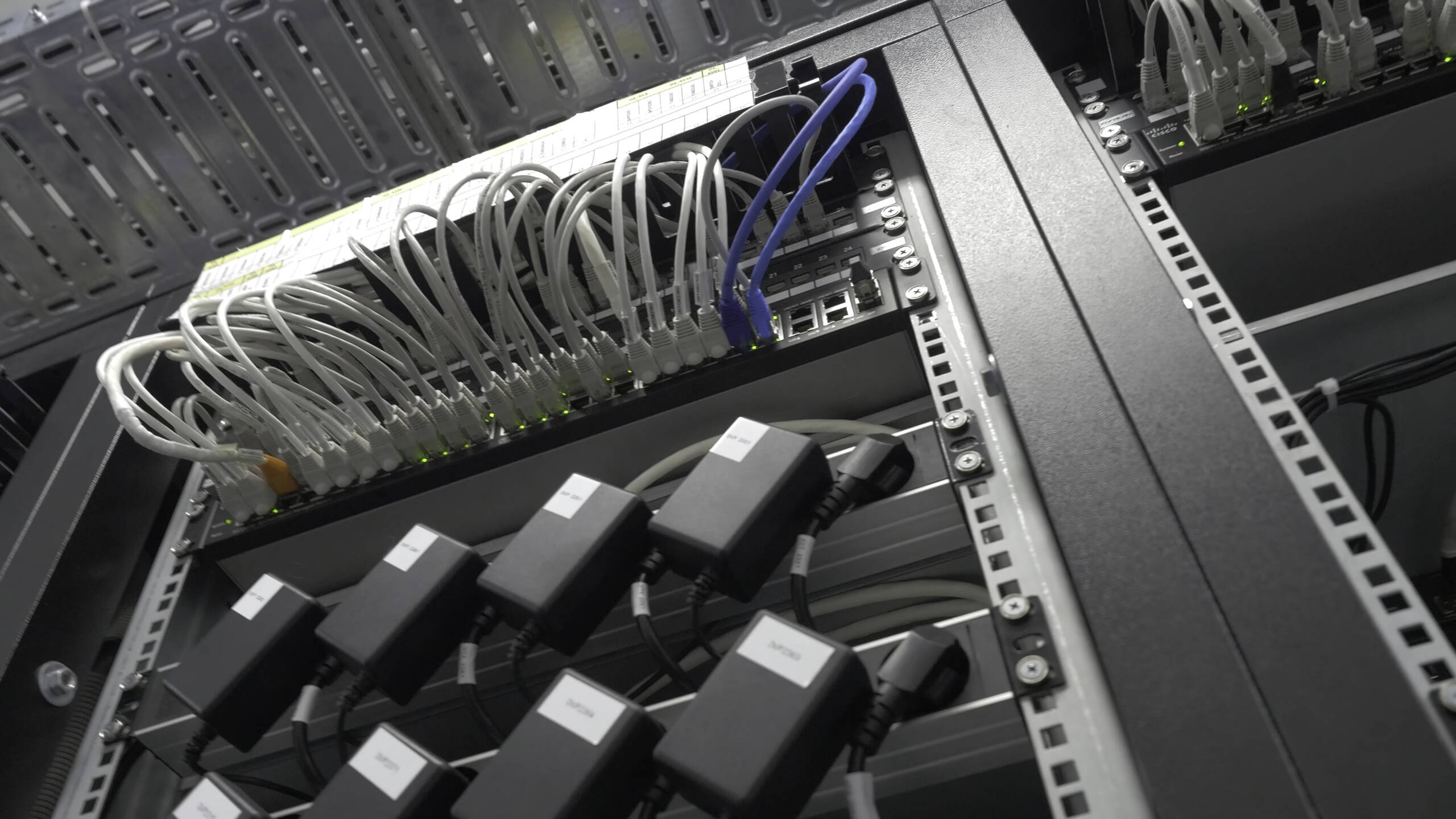 Netzwerkschrank mit Firewalls und Switches, sauber geführten Glasfaser- und Netzwerkkabeln und Kabelführungsbügeln