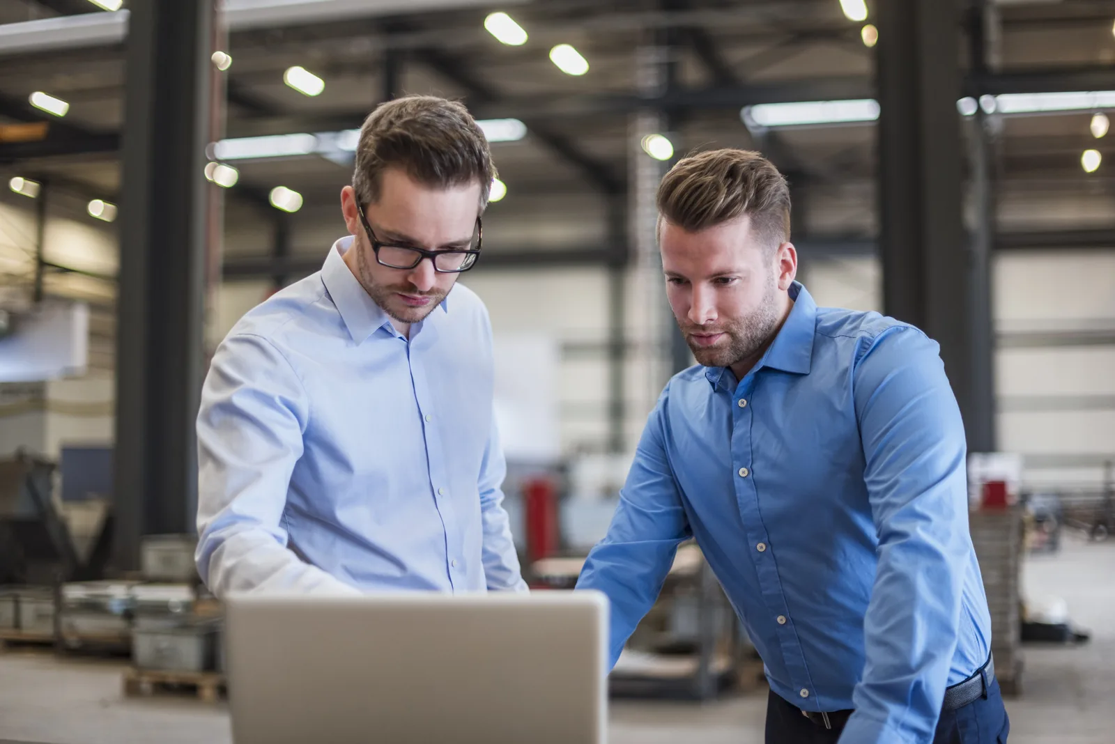 Zwei Geschäftsleute besprechen am Laptop in einer Produktionshalle die ERP-Einführung – Xentral Partner Delta One